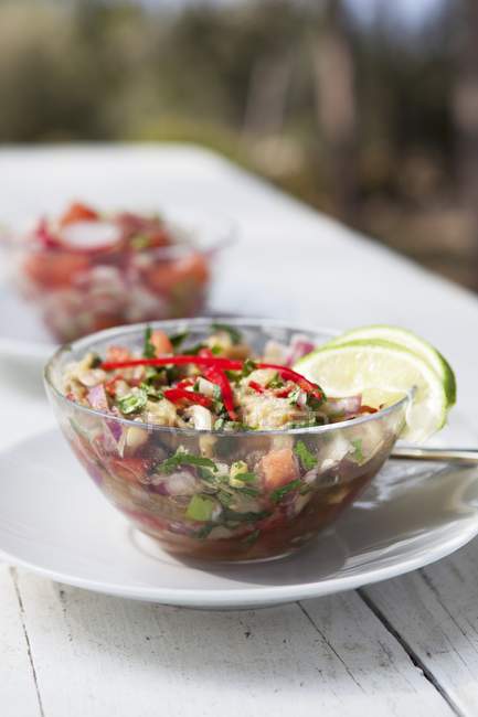 Auberginen-Paprika-Salat garniert mit Limetten auf weißem Teller über Holzoberfläche — Stockfoto