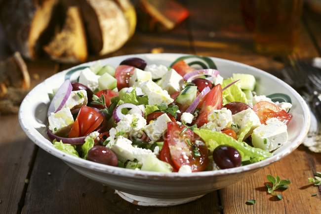 Греческий салат на белой тарелке на деревянной поверхности — стоковое фото
