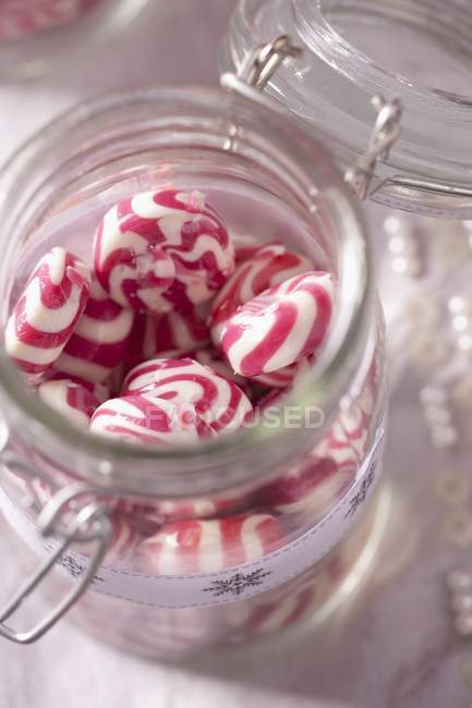 Vista de cerca de caramelos de menta roja y blanca en tarro de almacenamiento - foto de stock