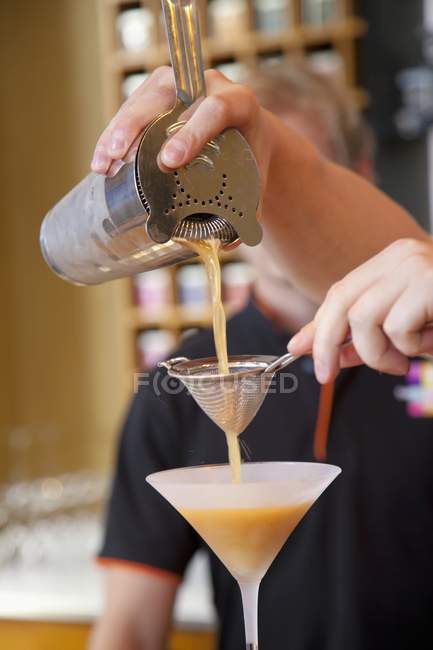 Vue découpée d'un homme versant du thé glacé d'un shaker dans un verre à cocktail — Photo de stock