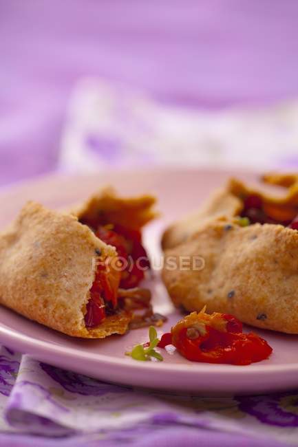 Wholemeal pastry parcels with pepper and onion filling, halved on purple plate — Stock Photo