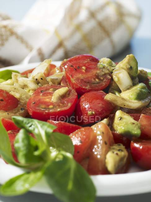 Tomato and avocado salad with onions and olive oil on white plate — Stock Photo