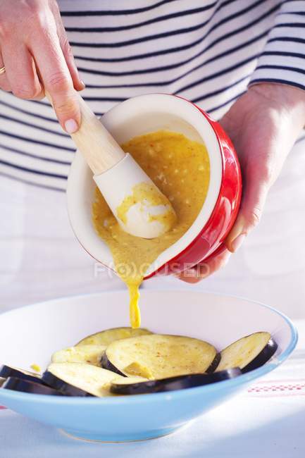 Une femme versant de la marinade à la moutarde sur de l'aubergine tranchée, au milieu — Photo de stock