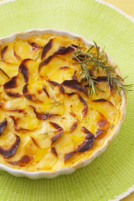 Potato gratin with rosemary on plate over green surface — Stock Photo