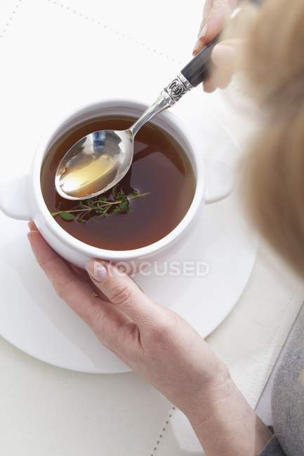 Elevated cropped view of a woman with a spoon of clear mushroom broth — Stock Photo