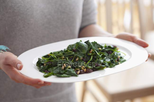 Person hält Gericht mit blanchiertem Spinat mit Rosinen und Pinienkernen — Stockfoto