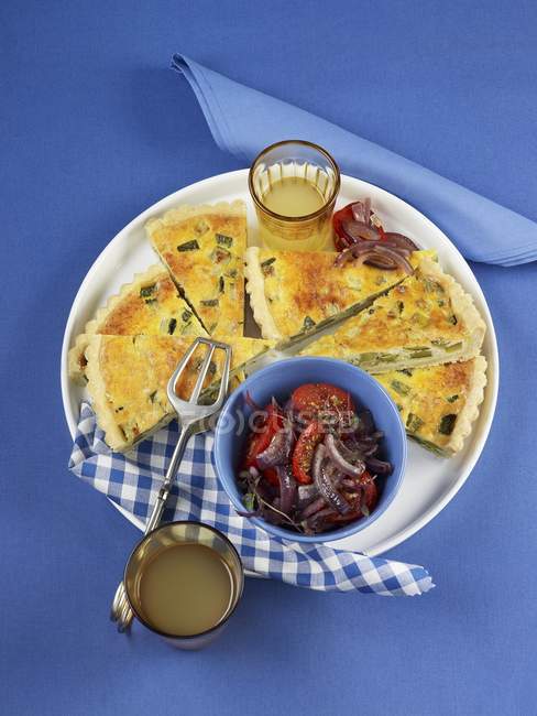 Courgette quiche with tomato and onion salad on white plate over blue surface — Stock Photo