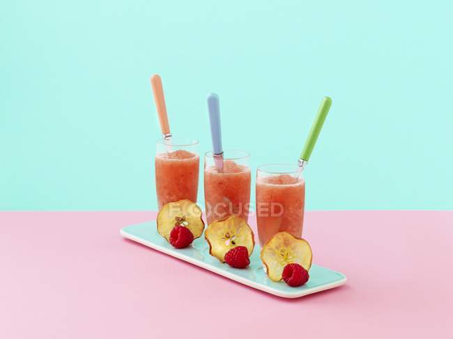 Closeup view of three glasses of pink apple frappe, decorated with slices of apple and raspberries — Stock Photo
