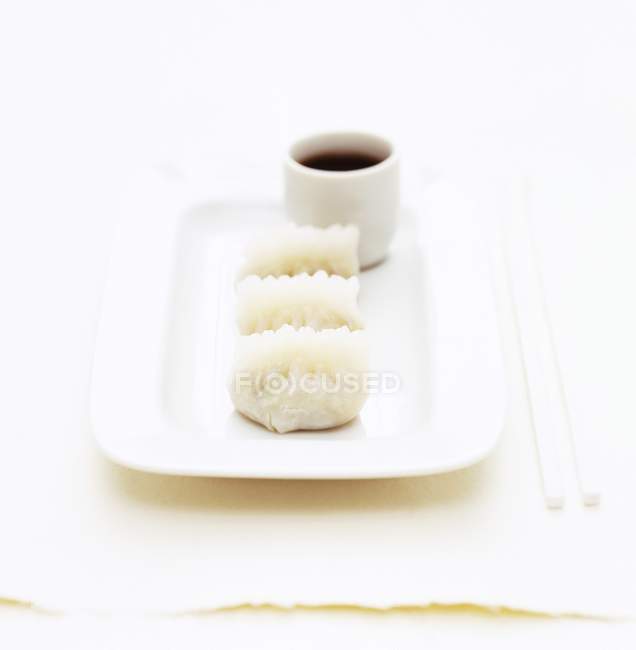 Vue rapprochée d'une assiette blanche avec trois boulettes et un ramequin blanc de sauce soja — Photo de stock