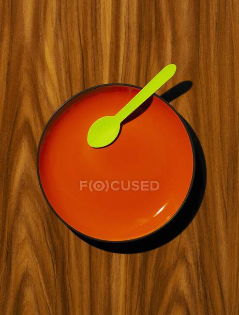 Red plate, with green wooden spoon on a wood effect background — Stock Photo
