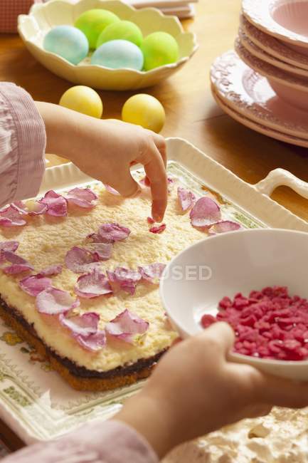 Vue recadrée de la personne décorant tarte Mazurek avec des pétales et des morceaux de fraises séchées — Photo de stock