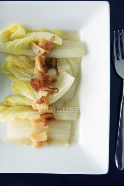 Steamed Chinese cabbage with scallops on white plate over black surface with fork — Stock Photo
