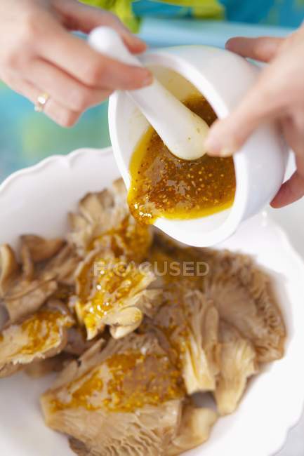 Closeup view of pouring mustard marinade over oyster mushrooms — Stock Photo