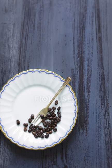 Кофейные зерна на тарелке с вилкой — стоковое фото