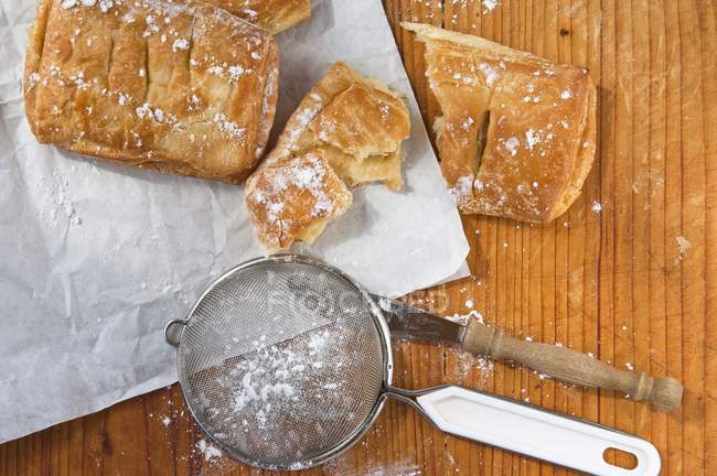 Closeup view of sieve with icing sugar and apple pastries — Stock Photo