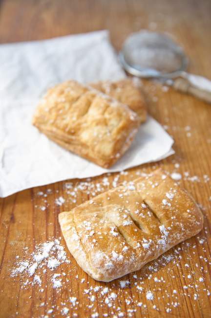 Apple pastries dusted with icing sugar over wooden surface — Stock Photo