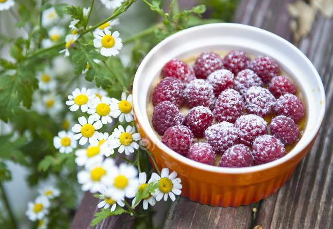 Closeup view of souffle with raspberries in bowl and daisies — Stock Photo