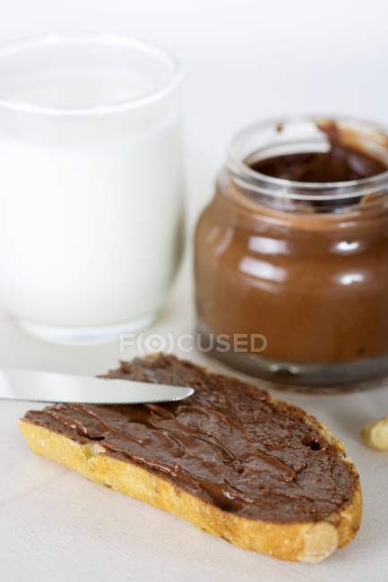 Closeup view of bread slice with chocolate spread and glass of mil — Stock Photo