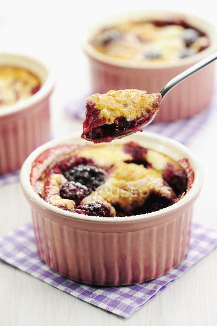 Closeup view of blackberry clafoutis in ramekins and on a spoon — Stock Photo