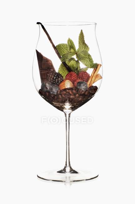 Vue rapprochée des baies, du chocolat, des grains de café, des noix et des herbes dans un verre à vin — Photo de stock