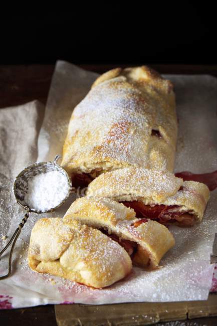 Peach strudel with icing sugar on baking paper — Stock Photo