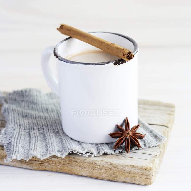 Vista de perto da caneca de esmalte branco de chá com pau de canela e anis estrelado em pano e placa de madeira — Fotografia de Stock