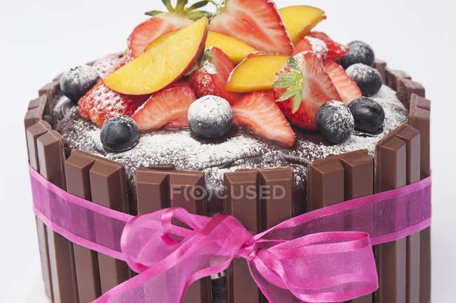 Primo piano vista della torta al cioccolato con frutta fresca, zucchero a velo e un nastro rosa — Foto stock
