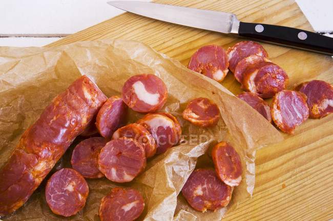 Vista elevada de fatias de Chorizo com uma faca em uma tábua de corte de madeira — Fotografia de Stock