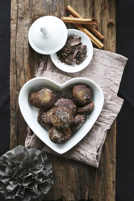 Vue du dessus des biscuits au chocolat et à la cannelle dans un bol en forme de cœur avec du chocolat râpé et des bâtonnets de cannelle — Photo de stock