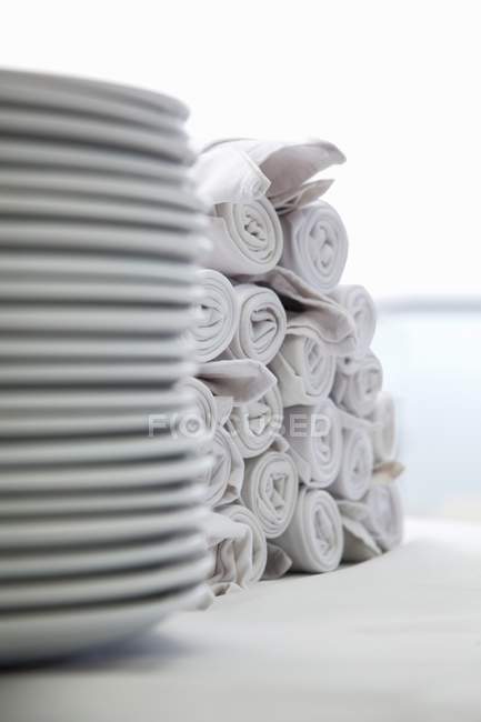 Closeup view of stacked white plates and heap of rolled napkins — Stock Photo