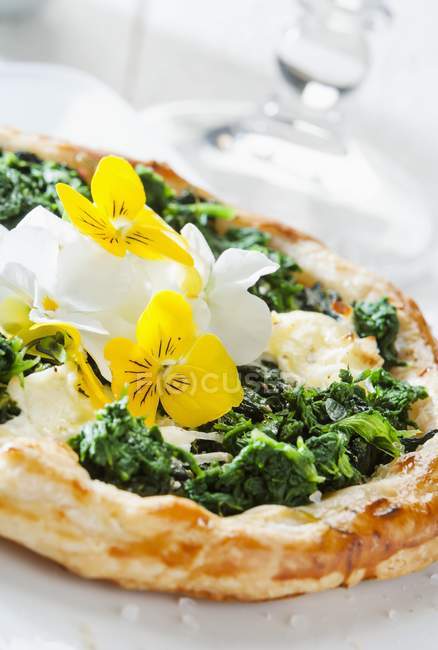 A spinach tart with edible flowers  on white plate — Stock Photo