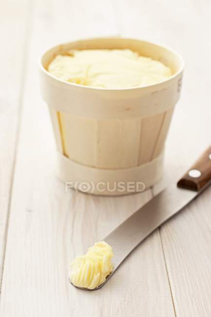 Closeup view of butter in a wood-chip basket and on a knife — Stock Photo