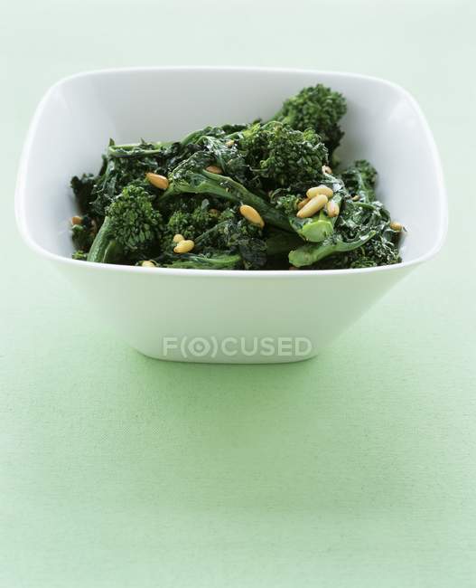 Sauted broccoli rabe in white bowl over green surface — Stock Photo