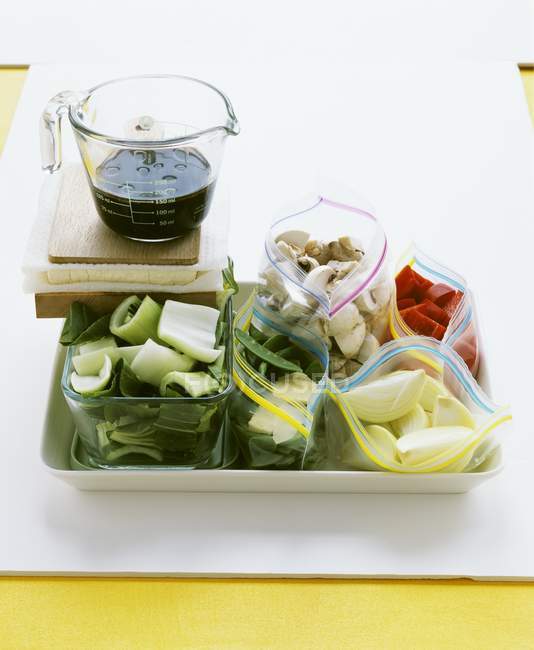 Tipos surtidos de verduras y champiñones en bolsas congeladoras en placa blanca sobre superficie blanca - foto de stock