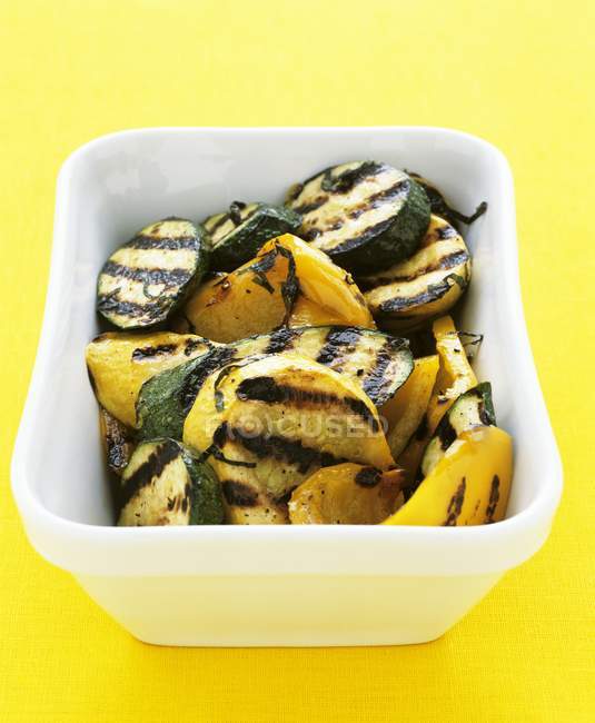 Gegrillte Zucchini und gelbe Paprika in weißer Schüssel über gelber Oberfläche — Stockfoto