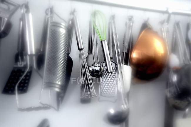 Vista de primer plano de utensilios de cocina surtidos colgando en la pared - foto de stock