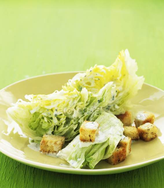 Closeup view of iceberg lettuce with croutons on green plate — Stock Photo