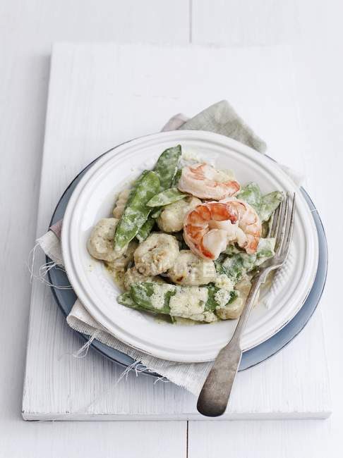 Saffron gnocchi with sugar snap peas and prawns  on white plate with fork — Stock Photo