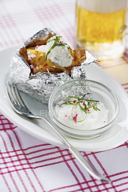 Pommes de terre cuites au four en papier d'aluminium, avec quark de radis sur une assiette avec fourchette — Photo de stock