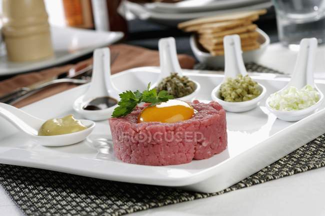 Closeup view of  raw meat stuffing with egg yolk, sauces and sliced vegetables — Stock Photo