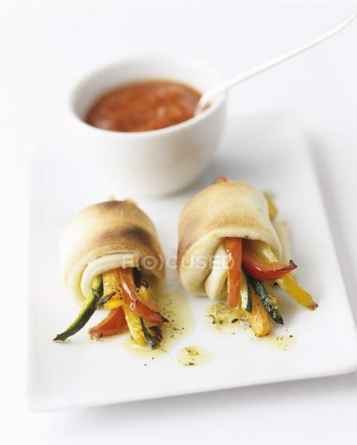Pan-fried vegetable batons wrapped in dough, with a tomato sauce on white plate over white surface — Stock Photo