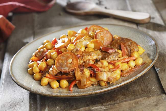 Ropa vieja guisado de grão de bico com salsicha, bacon, pimentas e tomates em prato sobre a superfície arborizada — Fotografia de Stock