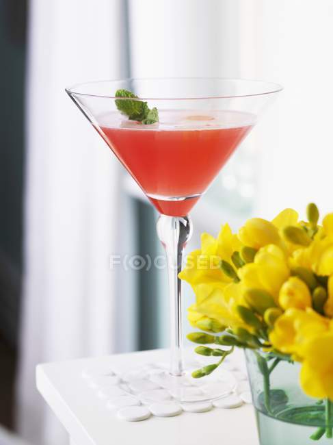 Vue rapprochée de la rhubarbe et de la menthe Caprioska en verre par des fleurs — Photo de stock