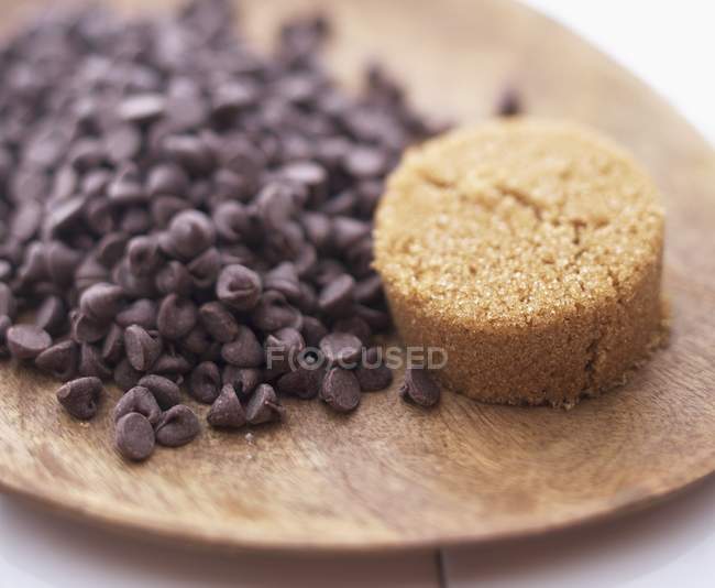 Closeup view of chocolate chips and brown sugar on wooden board — Stock Photo
