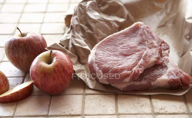 Chuletas de cerdo en papel de carnicero y manzanas - foto de stock
