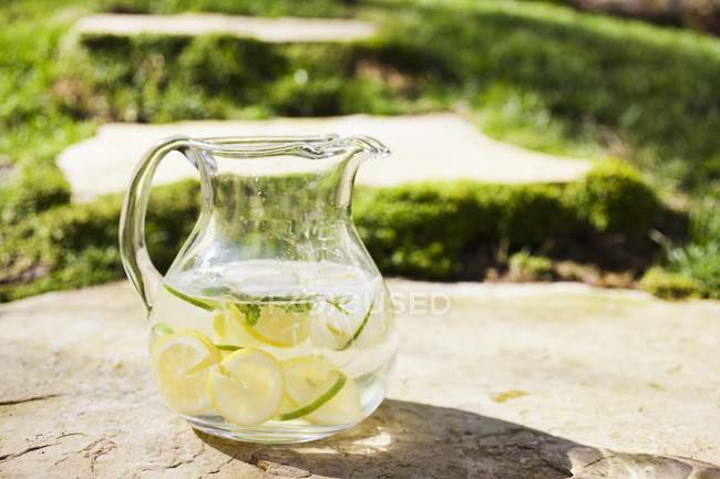 Глечик з водою скибочками лимона і вапно заморожений в кубики льоду — стокове фото