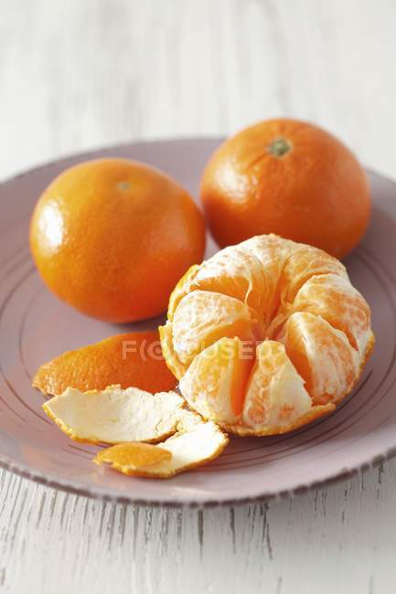 Whole and peeled mandarins on plate — Stock Photo