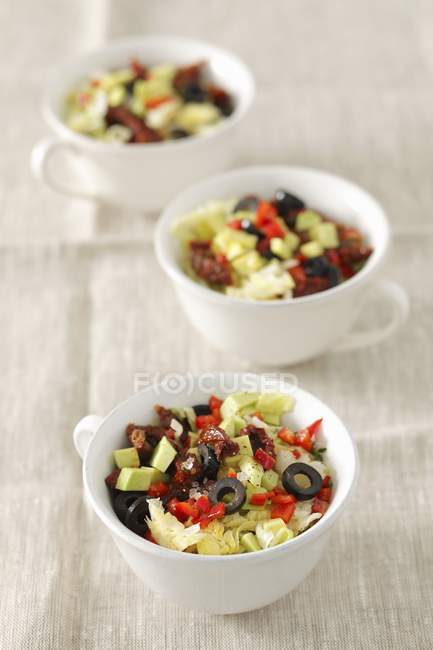 Iceberg lettuce with sundried tomatoes, avocado and olives in bowls — Stock Photo