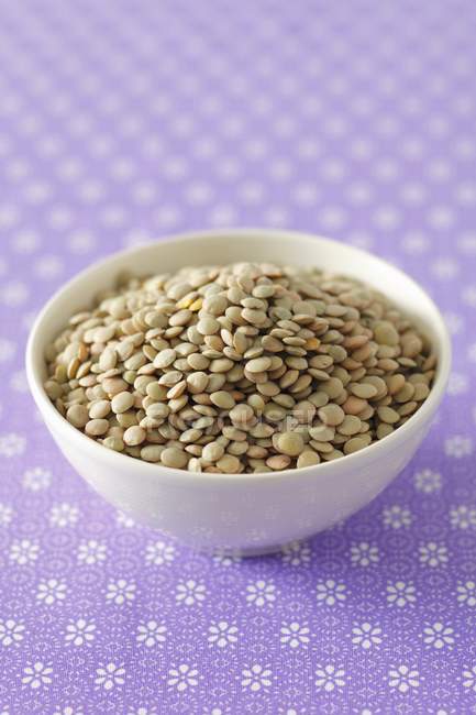 Closeup view of lentils in a white bowl on floral patterned purple surface — Stock Photo