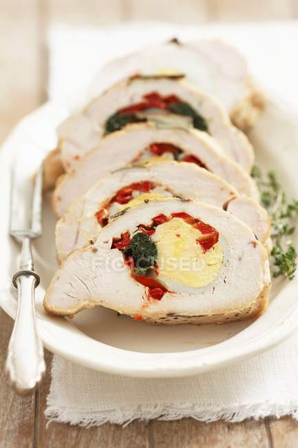 Грудь индейки, фаршированная яйцом, шпинатом и красным перцем на белой тарелке с вилкой — стоковое фото